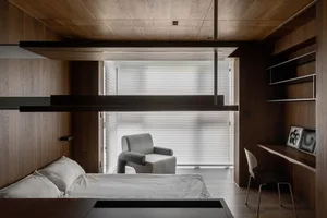 A modern bedroom featuring wooden furniture, a white armchair, and a desk with a computer monitor.