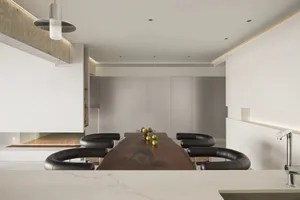 A minimalist dining room featuring a long wooden table with black chairs, surrounded by white walls and a fireplace.