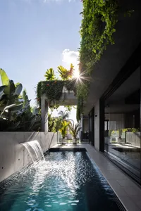 A modern pool with a waterfall feature, surrounded by concrete and lush greenery.
