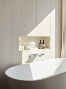 A minimalist bathroom featuring a white bathtub with a concrete wall and shelves.