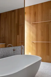 A minimalist bathroom with wooden walls and a white bathtub, featuring a hexagonal tile backsplash and sleek, modern fixtures