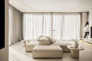 A minimalist living room featuring comfortable cushions, transparent blinds, and a modern design aesthetic.