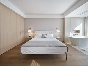 A contemporary white bedroom with minimalist design, featuring a white bed with wooden legs and a wooden wardrobe.