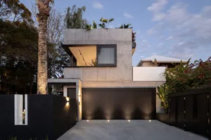 A modern concrete residence featuring a rooftop garden and black fence.