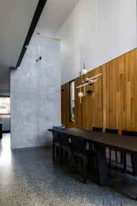 A modern dining room with concrete and wooden walls, black dining table and chairs, and contemporary white pendant lights.
