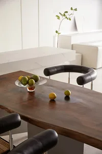 A modern dining space featuring a wooden table with a glass bowl of green and yellow fruits on it.