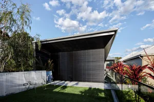 Modern house exterior featuring metal-clad walls and a flat roof under a blue sky with clouds.