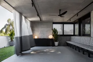 Modern living room with concrete walls, a bench with a geometric pattern, and potted plants.