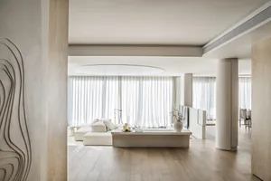 Minimalist living room with modern furniture, wood flooring, and large windows dressed in white curtains.