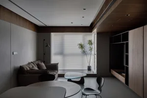 Modern living room with grey walls, black and grey furniture, and a potted plant in front of a large window.