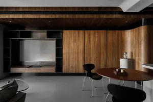 A modern residential interior featuring wood finishes, a minimalist dining area with a round wooden table and black chairs, a