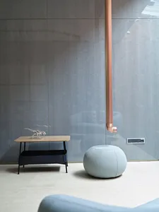 A modern living room featuring a metallic pipe and a small round pouf.