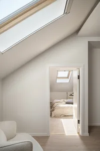 A minimalist bedroom featuring neutral-tones, white walls, and wooden elements with a skylight above, creating a serene and m