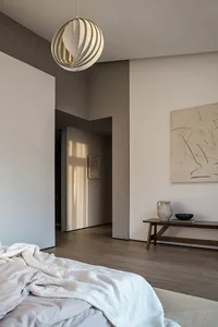 A minimalist bedroom featuring wooden furniture and a cotton blanket, with a modern light fixture and abstract artwork on the