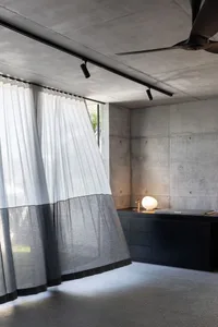 Contemporary minimalist office space with concrete walls and floors, featuring a sleek desk and modern table lamp.