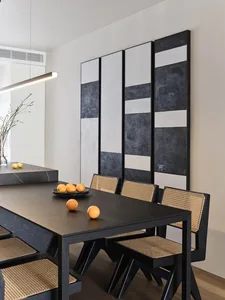 A modern dining room featuring a black table with oranges on it, and black and white abstract wall art.