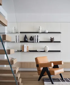 A modern living room featuring a minimalist bookshelf with decorative vases and books, and a comfortable leather armchair.