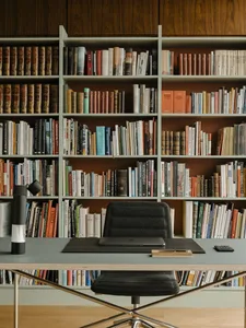 A home office with wooden shelves filled with books and a black desk with a laptop, chair, and lamp.