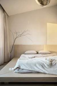 Minimalist bedroom featuring a platform bed with wood frame, white bedding, and a glass vase with a branch as decor.