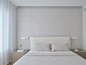 Minimalist bedroom featuring white fabric bedsheets and a wooden headboard.