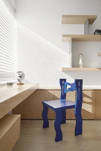 A modern home office featuring a blue chair with a unique, wavy design and a wooden desk and shelves.
