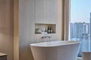 A modern bathroom featuring a marble bathtub in front of a large window with a city view.