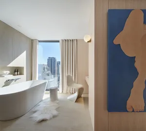 Modern bathroom featuring a freestanding bathtub, minimalist chair, and floor-to-ceiling windows with cityscape view.