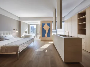 Modern minimalist bedroom with a wooden floor and furniture, featuring a large bed, a bathtub, and a painting on the wall.