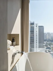 Modern bathroom featuring a sleek freestanding bathtub with water flowing from a wall-mounted faucet, overlooking the citysca