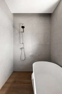 A minimalist bathroom with concrete walls features a modern shower head.
