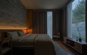 A minimalist bedroom featuring wooden elements and a large window with curtains.