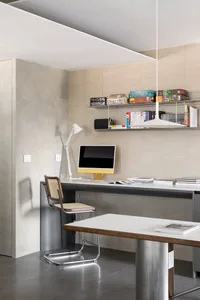A minimalist home office featuring a concrete desk, a wooden chair, and a white pendant light.