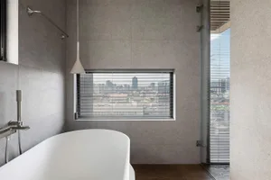 Modern bathroom with concrete tiles and blinds overlooking a city skyline.