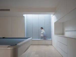 A modern dwelling featuring glass cabinets and a white wooden floor with a person walking in the background.
