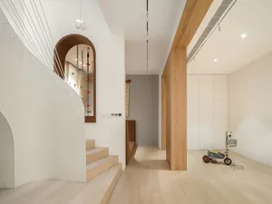 A modern residential interior featuring a living room area with a concrete column, light-colored wood paneling, and a small c