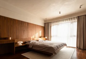 A modern minimalist bedroom with wooden walls, a bed with light-colored bedding, and large windows with curtains.