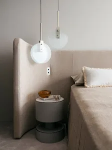 Modern minimalist bedroom featuring a fabric headboard and beige bedspread, with a side table holding a crystal tray and an a