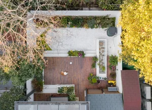 Aerial view of a modern minimalist garden featuring a wooden deck, concrete patio, and assorted plants.