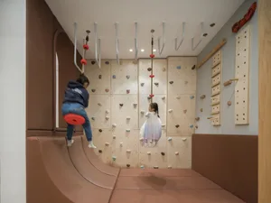 Children playing on a wooden climbing wall and slide in a playroom