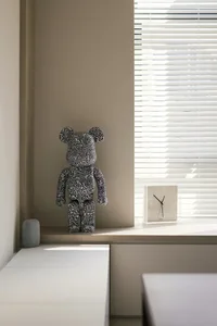 A minimalist desk area featuring a patterned teddy bear, a clock, and a white side table.