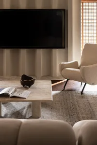 A minimalist living room with white walls, a wooden floor, a stone coffee table, and a white fabric armchair.