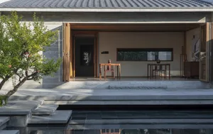 Concrete exterior of a minimalist residential house, featuring open doors and a serene outdoor pool and garden.