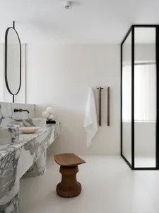 Modern minimalist bathroom with marble sink and floor, and a wooden stool.