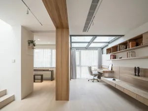 A modern home office featuring a light-colored wooden desk, chair, and shelves with books and decor items.