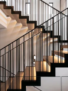 A modern industrial staircase made of concrete with black metal railings, illuminated by soft lighting against a white wall b