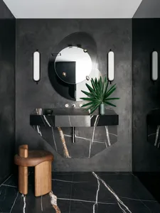A modern bathroom with a black marble sink and a round mirror.