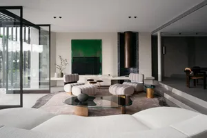 A modern minimalist living room with concrete walls, glass coffee table, and comfortable seating.