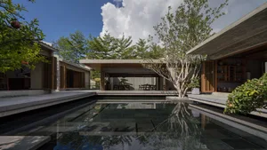 Modern residential pool with concrete walls and floors, surrounded by greenery, under a blue sky with clouds.