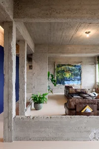 An industrial-style living room featuring exposed concrete walls and ceiling, a leather sofa, and a large abstract painting.