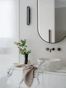 A minimalist bathroom featuring a marble counter with a vase, bowl, and towel hanging on it.